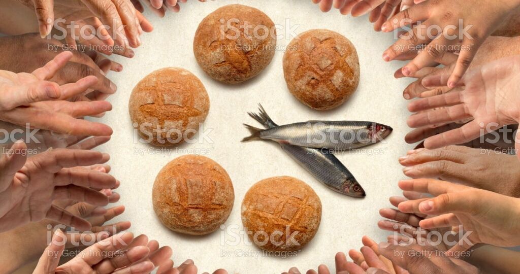 Many hands stretching around five small barley loaves and two small fish